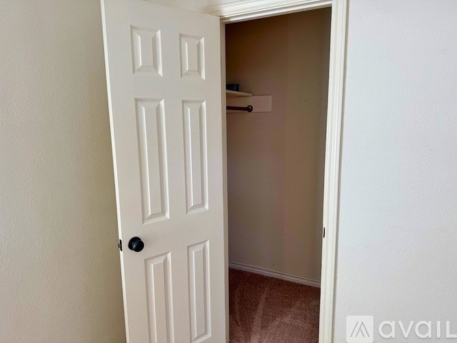 A white door with a black handle is open to a small, empty room.