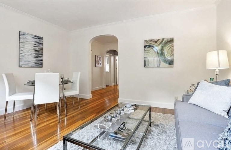 A living room with a grey couch, a glass coffee table, and a dining table with chairs.