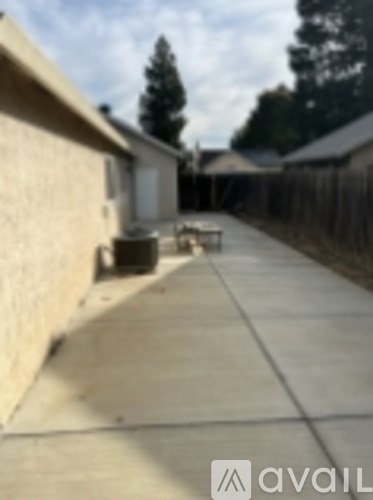 A concrete walkway leads to a house with a tree in the background.
