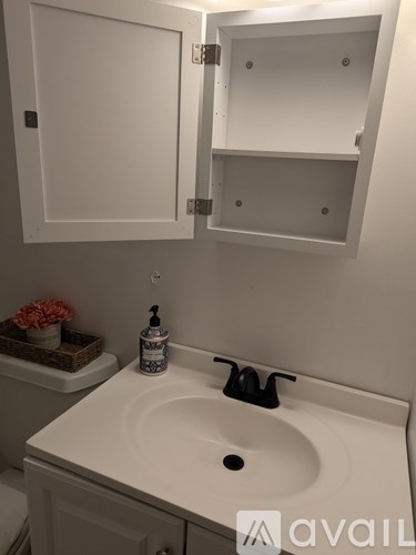 A white bathroom sink with a black faucet and a white cabinet above it.