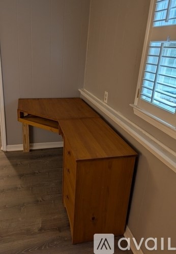 A wooden desk with a drawer is in a room with a window.