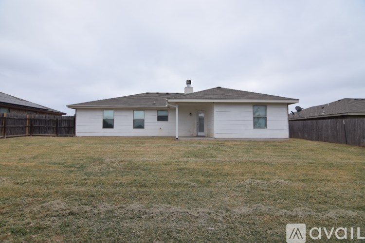 A house with a brown roof and a white exterior is surrounded by a fence and a grassy yard.