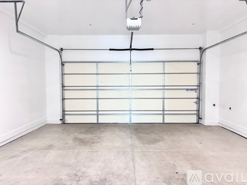 A large, empty garage with a roll-up door and a ceiling fan.
