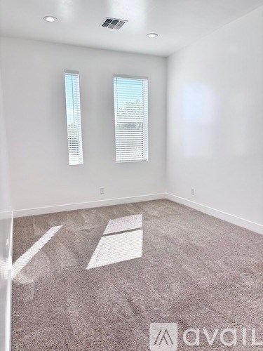 A room with carpeted floor and two windows.