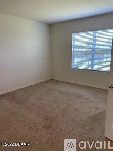 A room with a carpeted floor and a window with blinds.