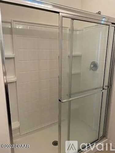 A glass shower door in a white tiled bathroom.