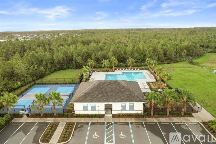 A building with a swimming pool surrounded by trees and a parking lot with handicap spaces.