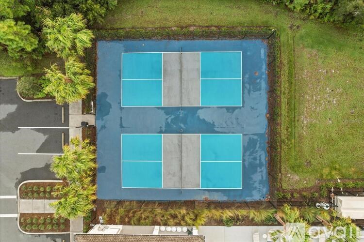 An aerial view of a tennis court surrounded by trees and a parking lot.