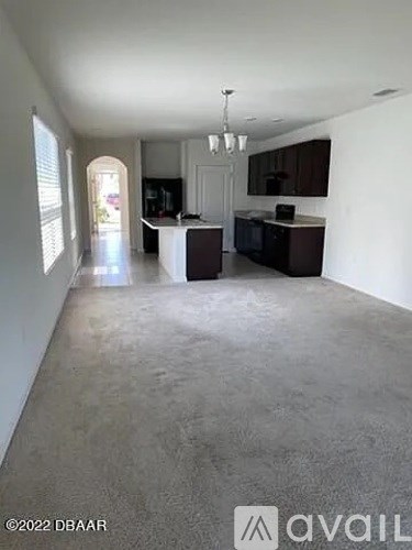 A spacious living room with a kitchen area in the background.