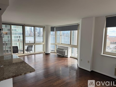A spacious living room with wooden floors and large windows overlooking a cityscape.