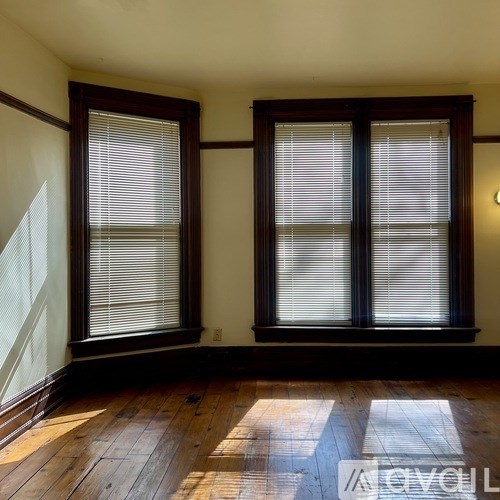 A room with wooden floors and two windows with blinds.