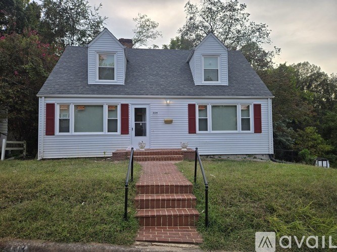A white house with red trim and a brick walkway leading to the front door.
