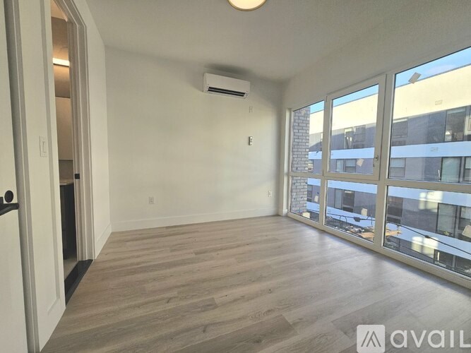 A spacious room with wooden flooring and large windows.