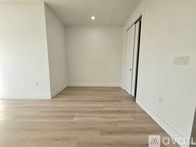 A room with wooden flooring and white walls, with a door on the right side.