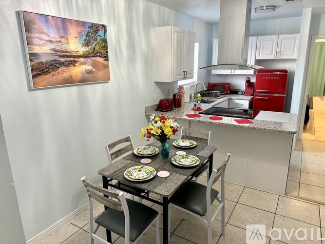 A kitchen with a table set for two and a painting of a beach scene on the wall.