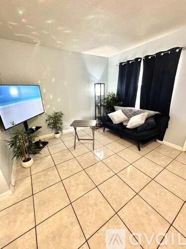 A living room with a black couch, a television, and a potted plant.
