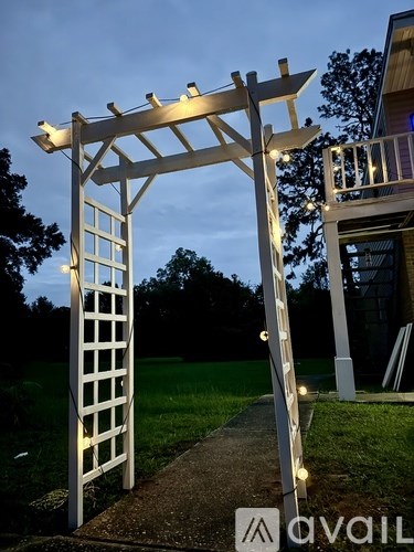 A white wooden pergola with lights is in front of a house.
