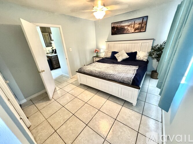 A bedroom with a bed, a ceiling fan, and a painting on the wall.