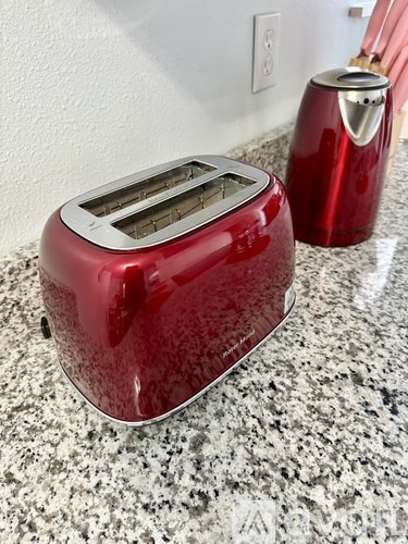 A red toaster is on a granite countertop.