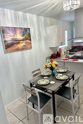 A kitchen with a table set for two and a painting of a beach scene on the wall.