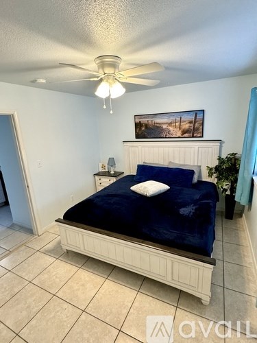 A bedroom with a bed, a ceiling fan, and a painting on the wall.