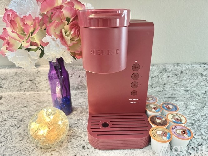 A Kefir machine is pink and sits on a marble surface with a vase of flowers and a candle nearby.