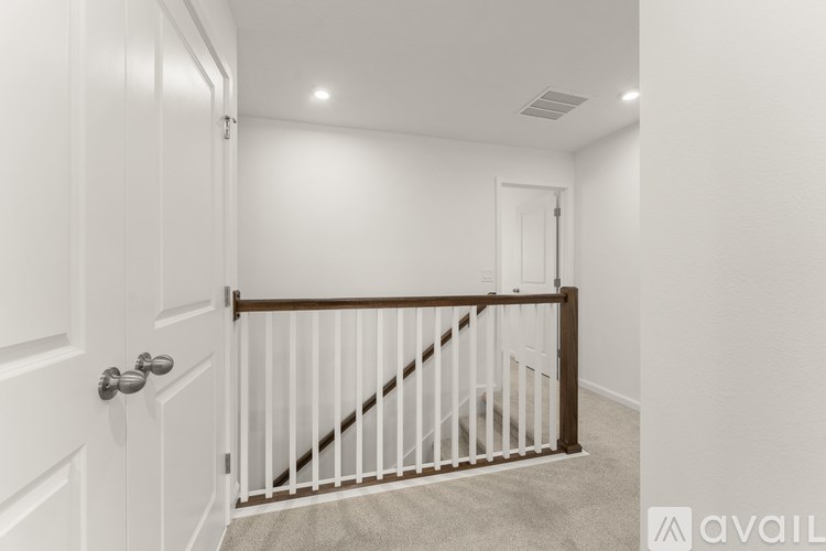 A hallway with a carpeted floor, a white door, and a wooden staircase.