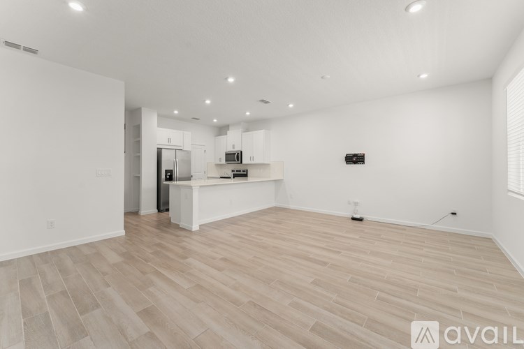 A spacious room with wooden flooring and a kitchen area in the background.