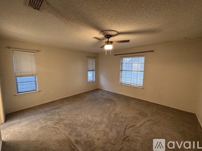 A room with a carpeted floor, a ceiling fan, and two windows.