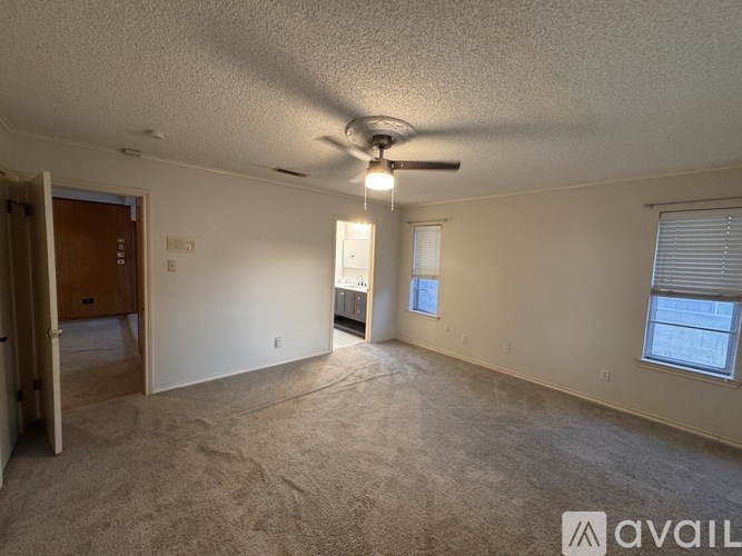 A spacious room with a ceiling fan and two windows.
