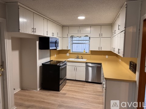 A kitchen with a black fridge, white cabinets, and a yellow counter.