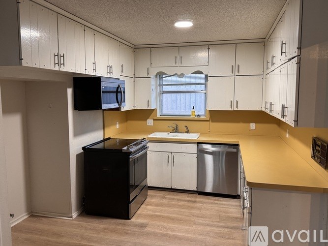 A kitchen with a black fridge, white cabinets, and a yellow countertop.