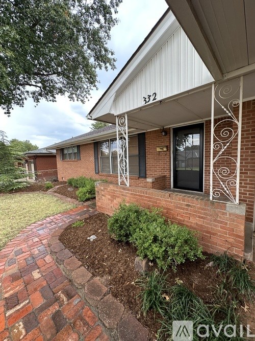 A house numbered 372 with a white porch and a brick wall.