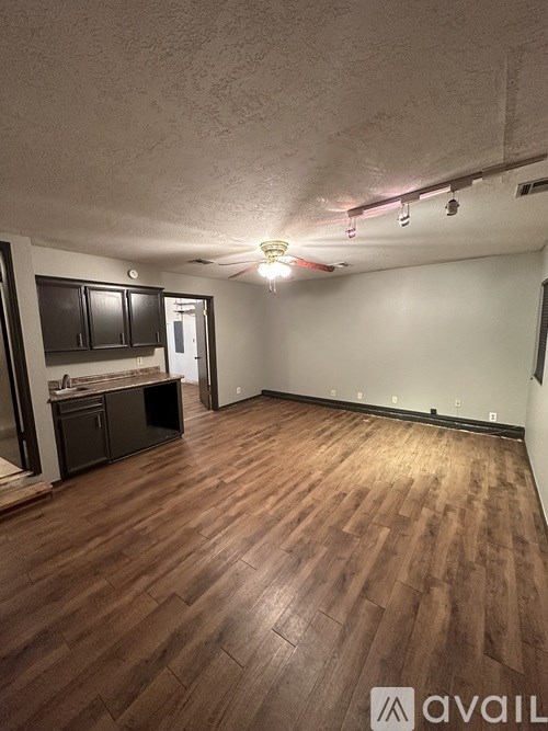 A room with wooden flooring and a kitchen area with black cabinets.