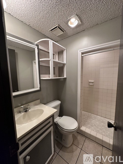 A bathroom with a toilet, sink, mirror, and a shower.