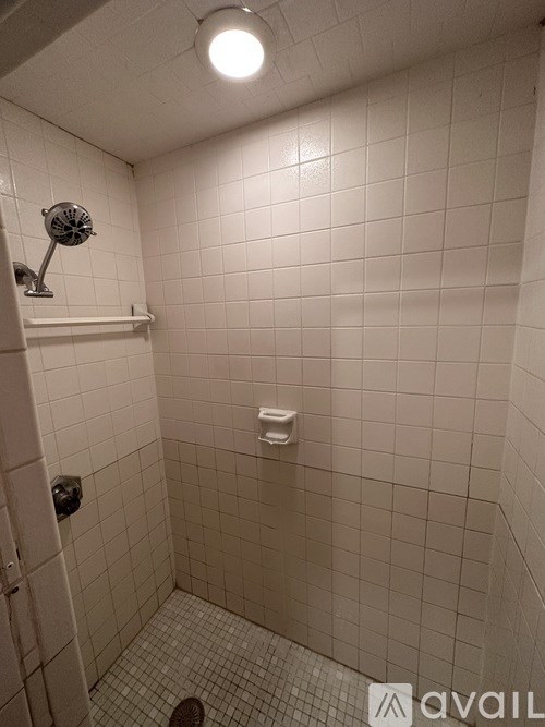 A small, white tiled bathroom with a shower head and a toilet.
