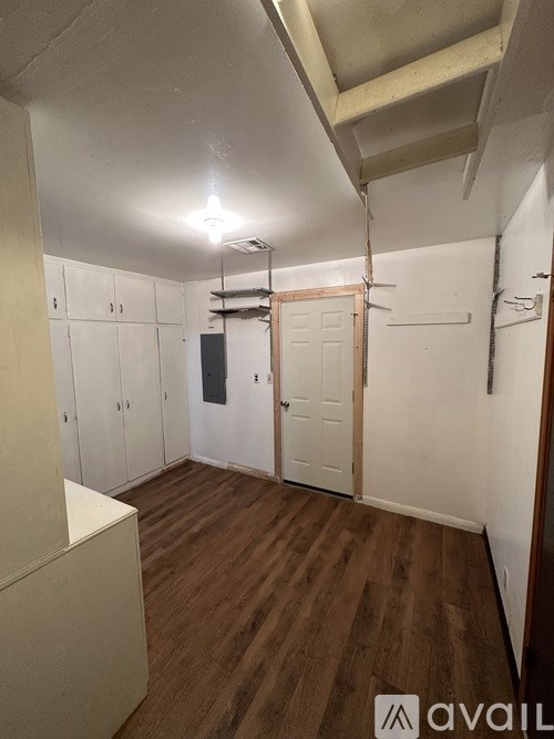 A room with wooden floors and white walls, with a door and a cabinet.