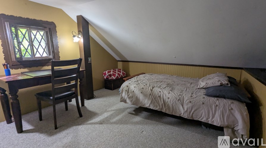 A bedroom with a bed, desk, chair, and window.
