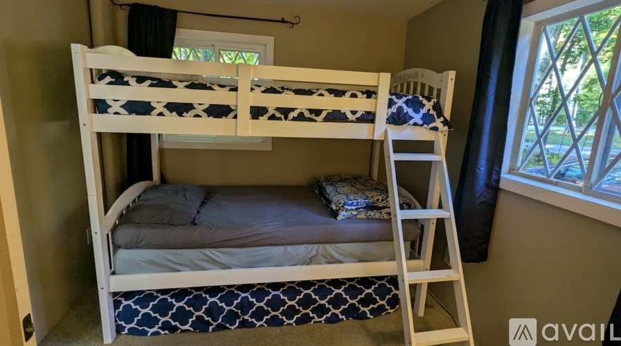 A white bunk bed with a ladder is in a room with a window.