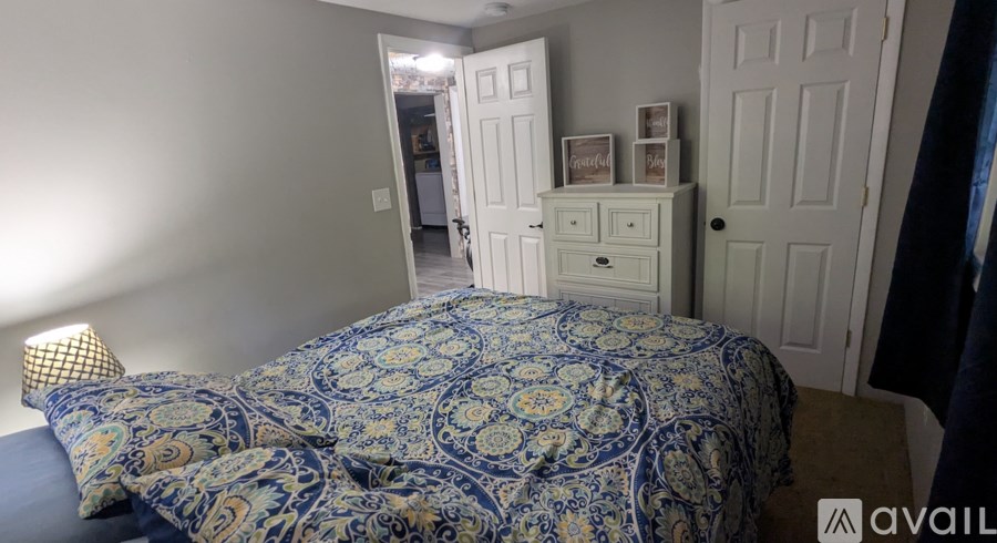 A bedroom with a patterned bedspread and a white dresser.