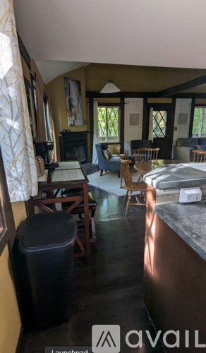 A black trash can sits in a kitchen with a black stove and black chairs.