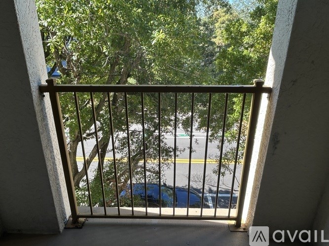 A balcony with a metal railing overlooks a parking lot and trees.