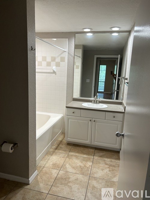 A bathroom with a white tub, sink, and tiled floor.
