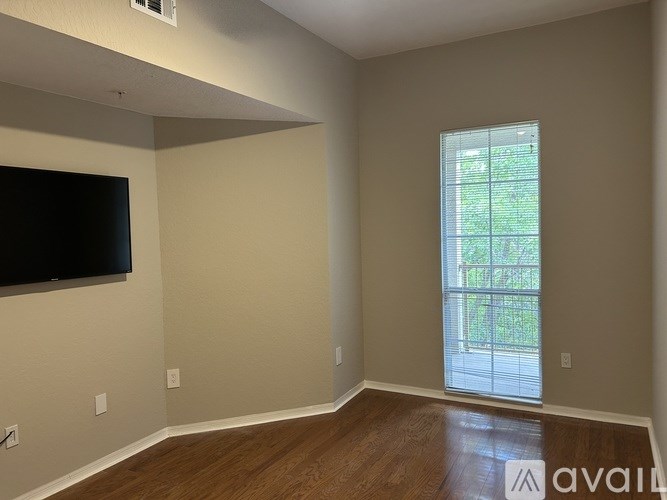A room with a flat screen TV mounted on the wall and a window with blinds.