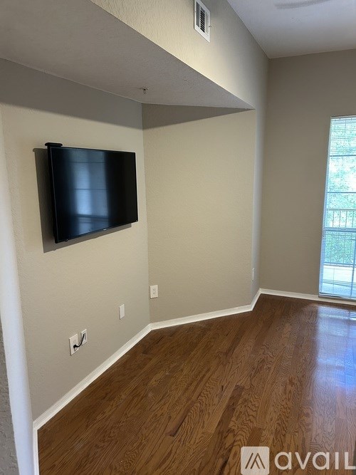 A black TV is mounted on a wall above a wood floor.