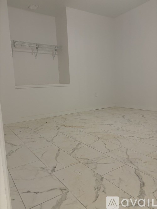 A room with marble flooring and a white wall with a coat rack.
