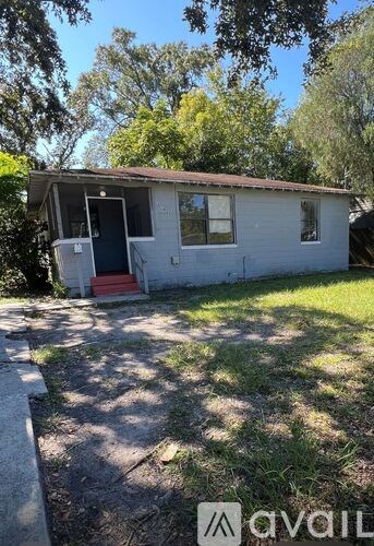 A small white house with a red door and a shadow of a tree on the ground.