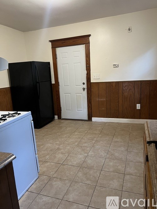 A kitchen with a black refrigerator, white door, and a white stove top oven.