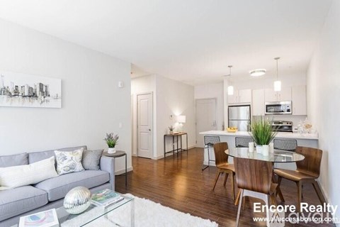 A living room with a grey couch, a glass coffee table, and a dining table with chairs.