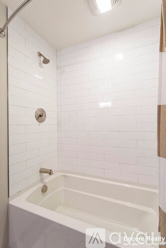 A white tiled bathroom with a white bathtub and a shower head.